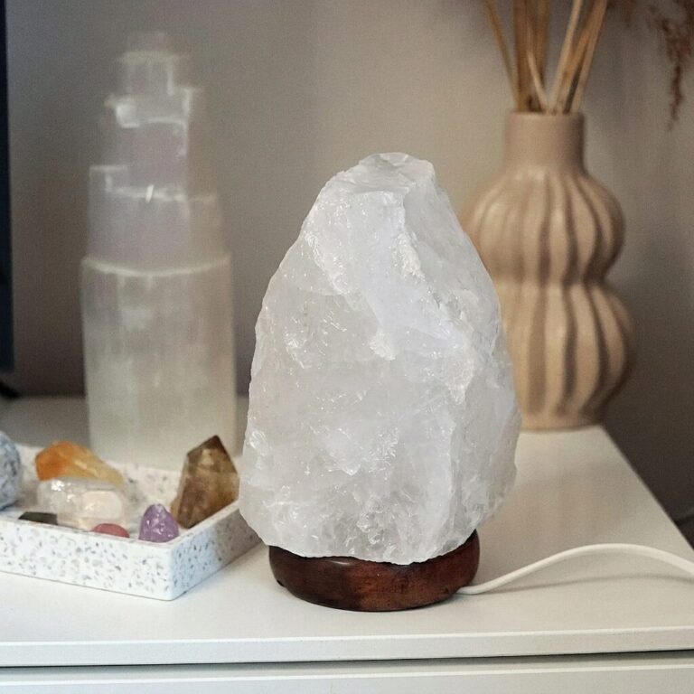 Lampa z surowej były naturalnego kryształu górskiego na drewnianej podstawie, stojąca na jasnej szafce.
